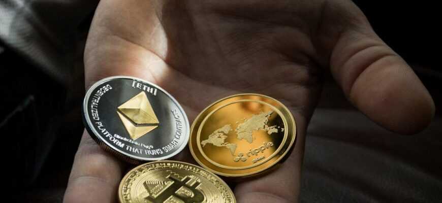 Hand holding Bitcoin, Ethereum, and Ripple coins representing digital currency.