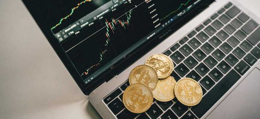 Golden bitcoin coins placed on a laptop keyboard with trading chart displayed on the screen.