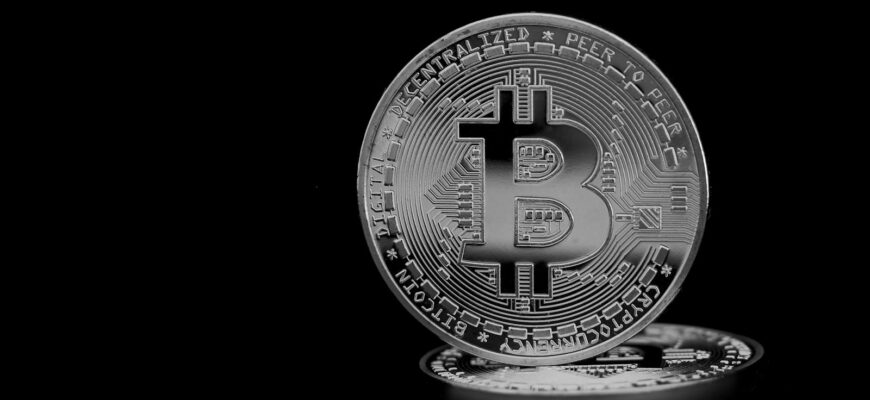 Close-up of a silver bitcoin coin, highlighting the cryptocurrency symbol on a black background.